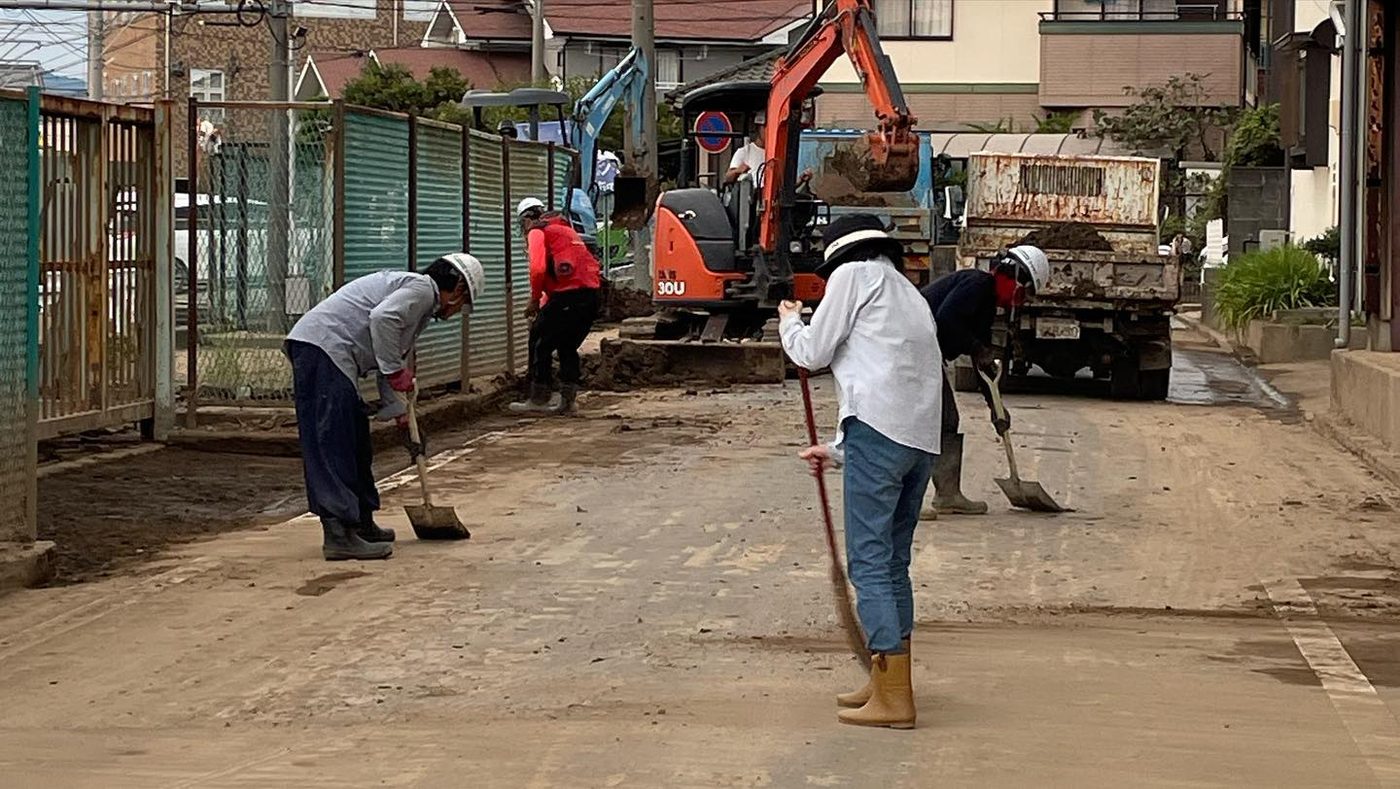 A residential street with people digging out mud and heavy machinery