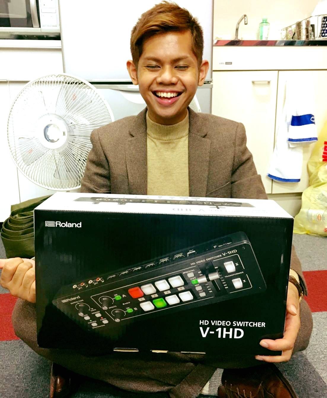 Narita Jun laughing as he carries a box of live-streaming equipment
