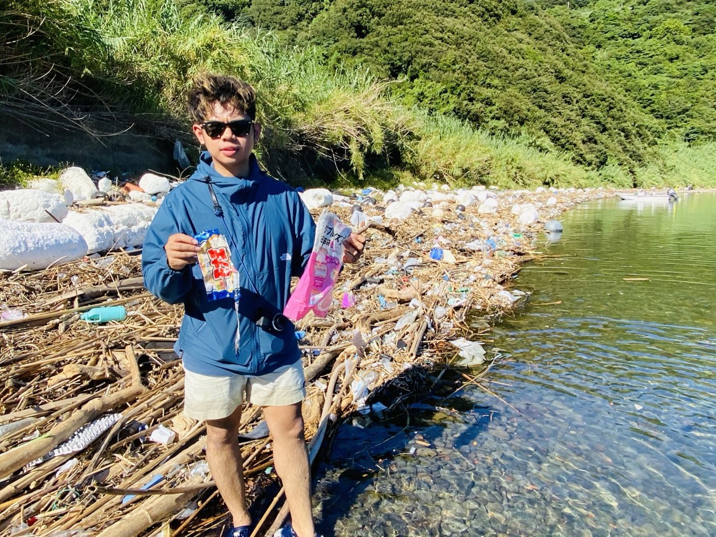 Narita Jun holding litter he picked up on a shore strewn with ocean trash