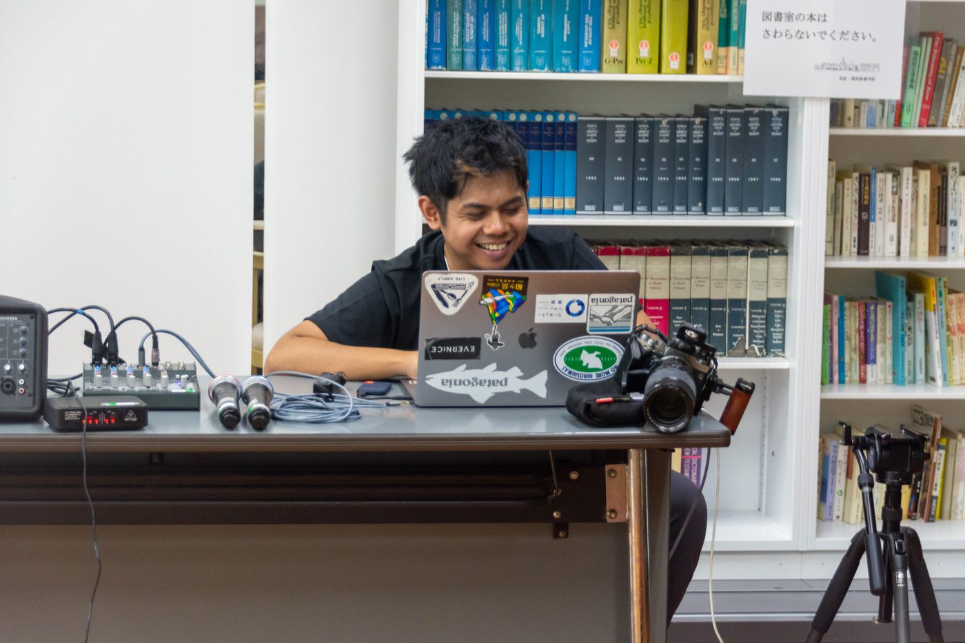Narita Jun at his computer and camera in front of a bookshelf
